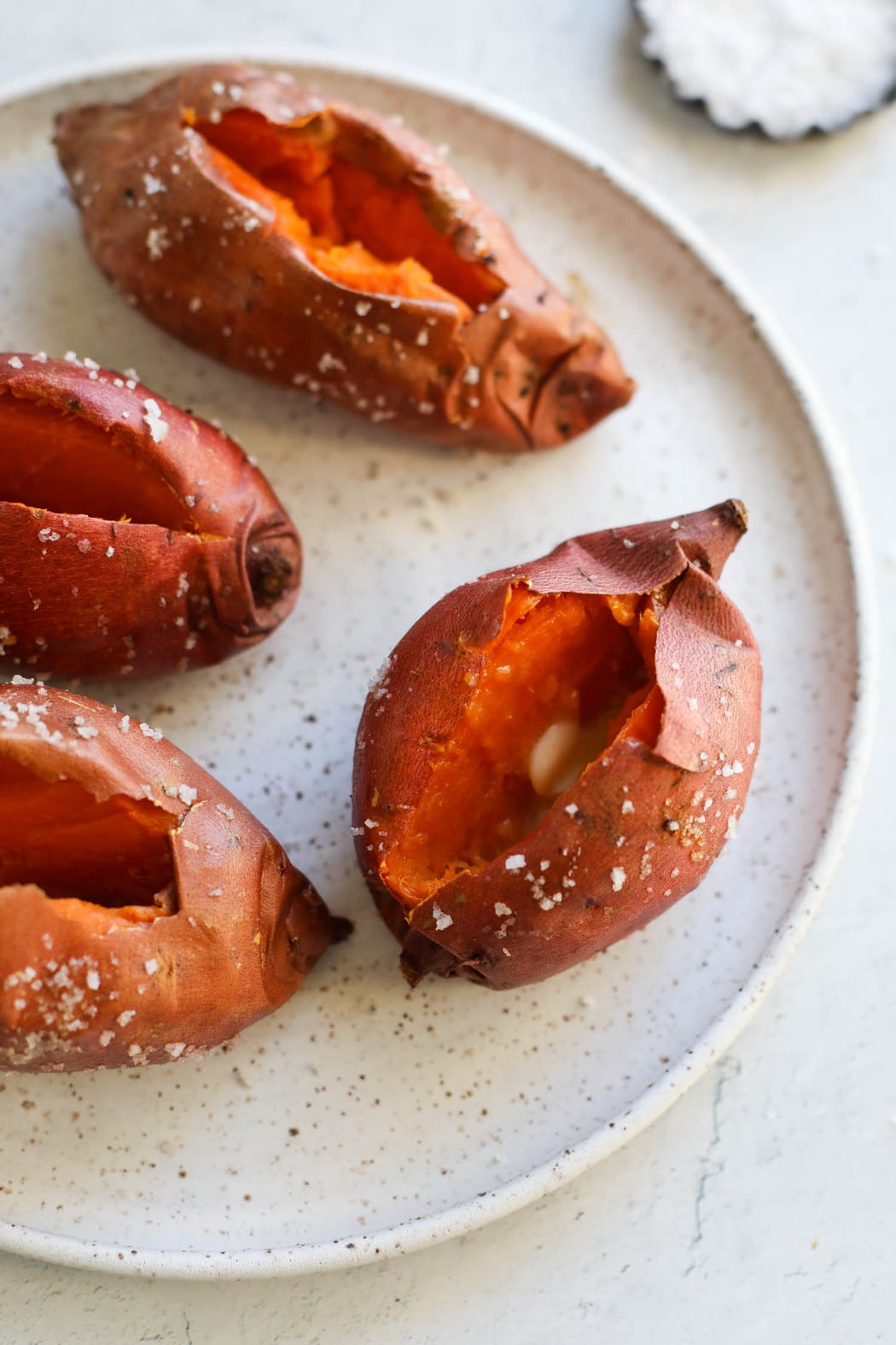 Baked sweet potatoes on stone platter with cut down middle to show inside orange flesh