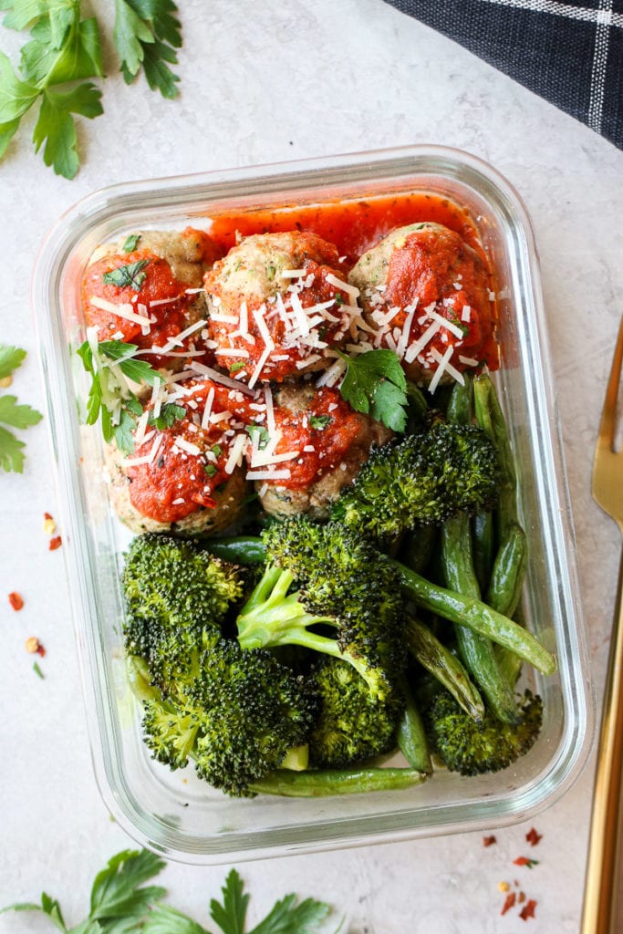 Overhead view of a glass meal prep container filled with Italian Turkey Zucchini Meatballs, broccoli, and green beans.