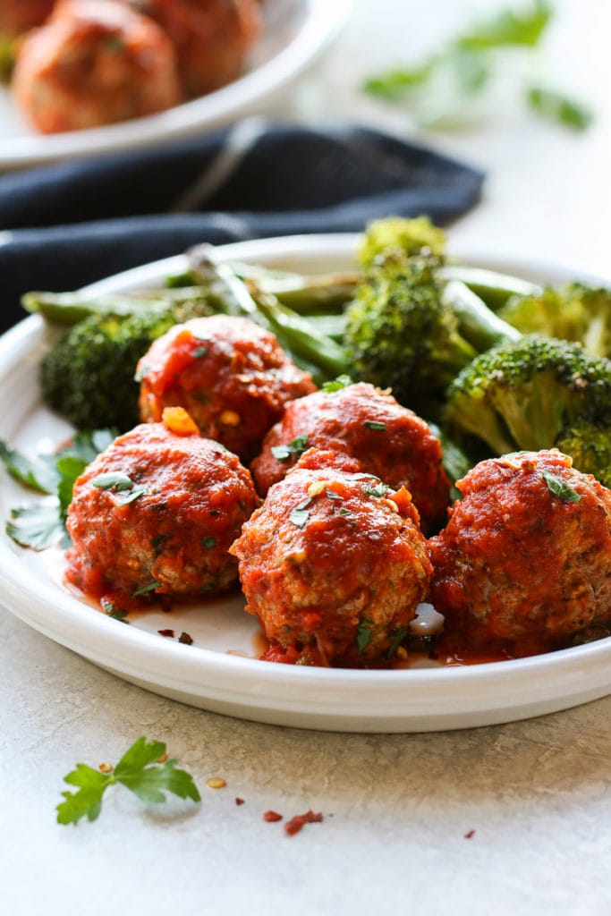 A close-up view of a plate of Turkey Zucchini Meatballs with a side of broccoli.