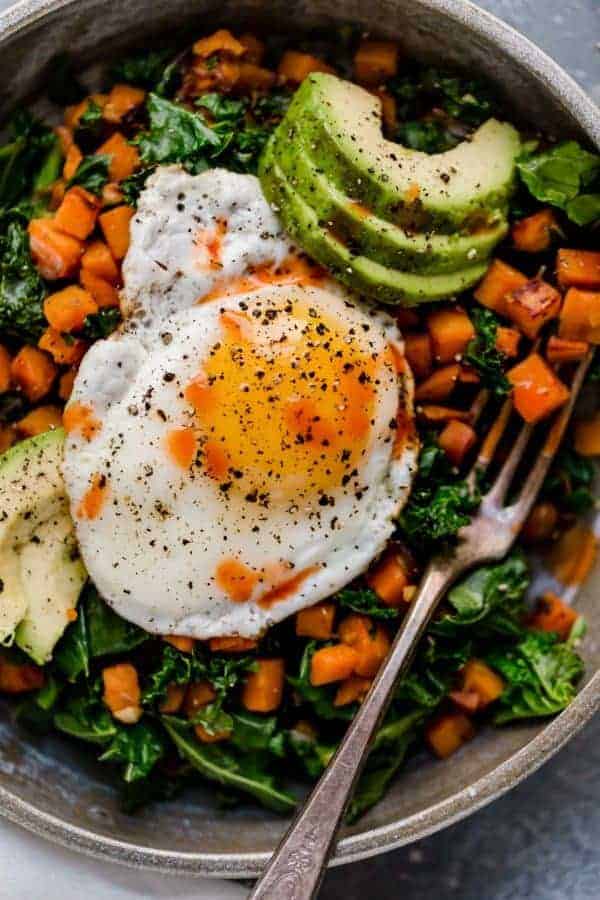 Overhead shot of Kale and Sweet Potato Sauté in a bowl with a fried egg on top and avocado slices.
