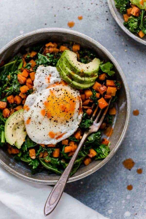 Overhead shot of Kale and Sweet Potato Sauté in a bowl with a fried egg on top and avocado slices.