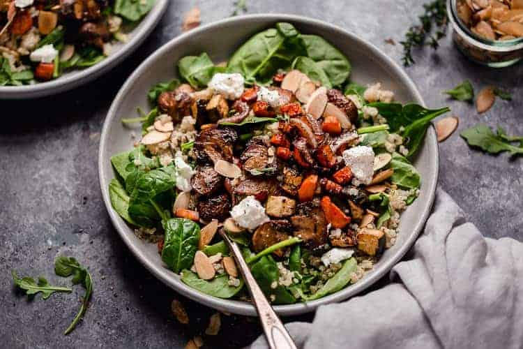 Side view balsamic roasted vegetables over quinoa salad and mixed greens in shallow bowl.