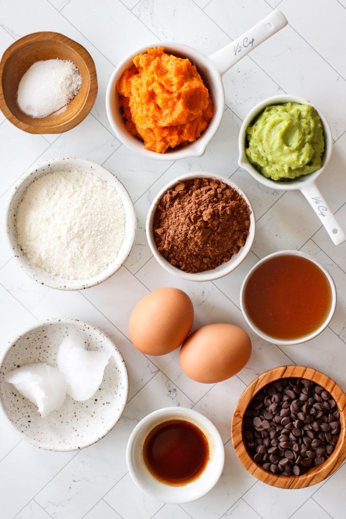 Overhead view of all ingredients for grain-free sweet potato avocado brownie bites arranged in small bowls and measuring cups.