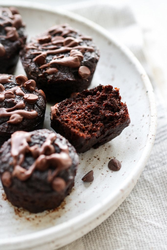 Close up view of a half a grain-free sweet potato avocado brownie bite with cake-like texture on a speckled plate with more brownie bites.