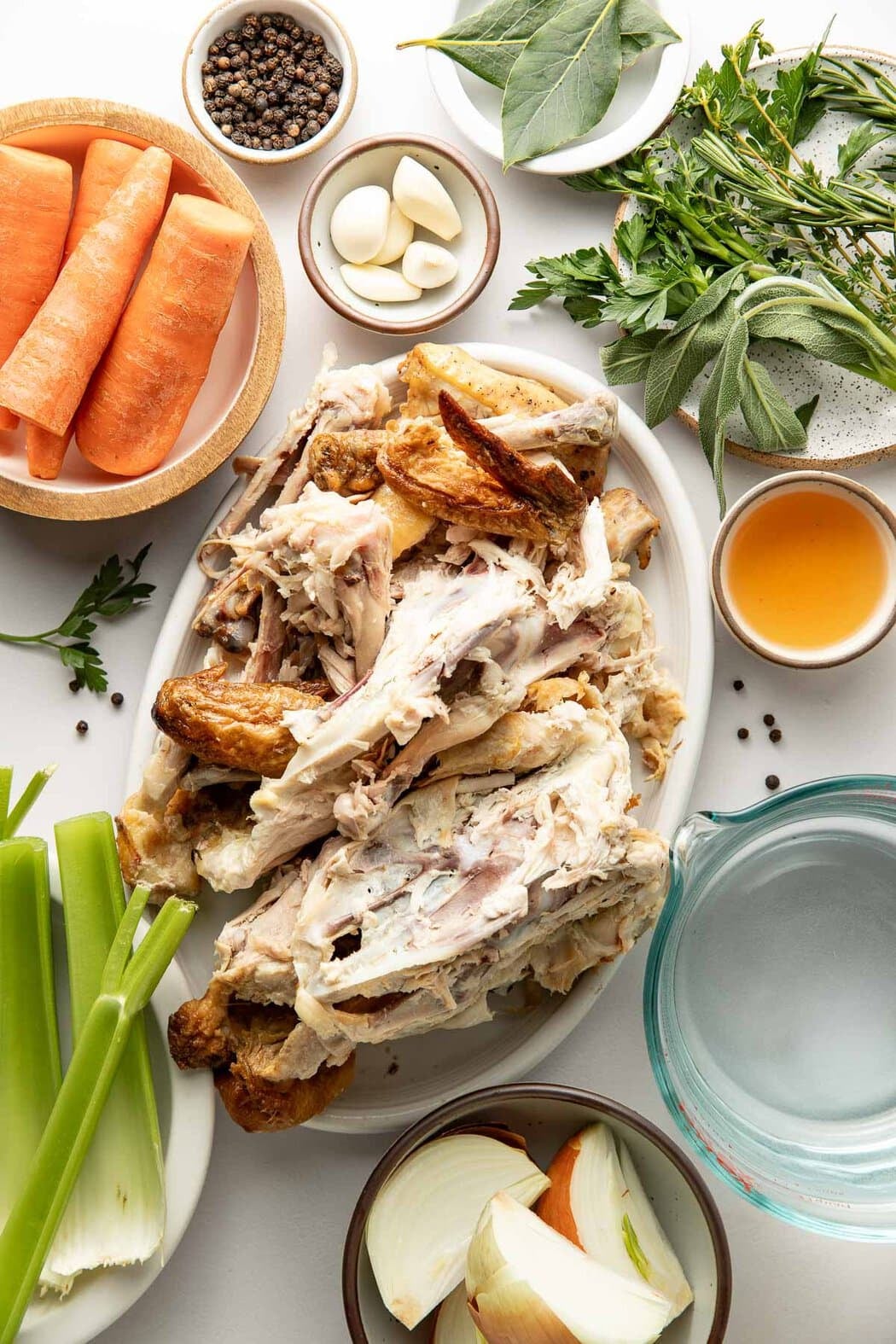 Overhead view of a variety of ingredients for bone broth on a white countertop.