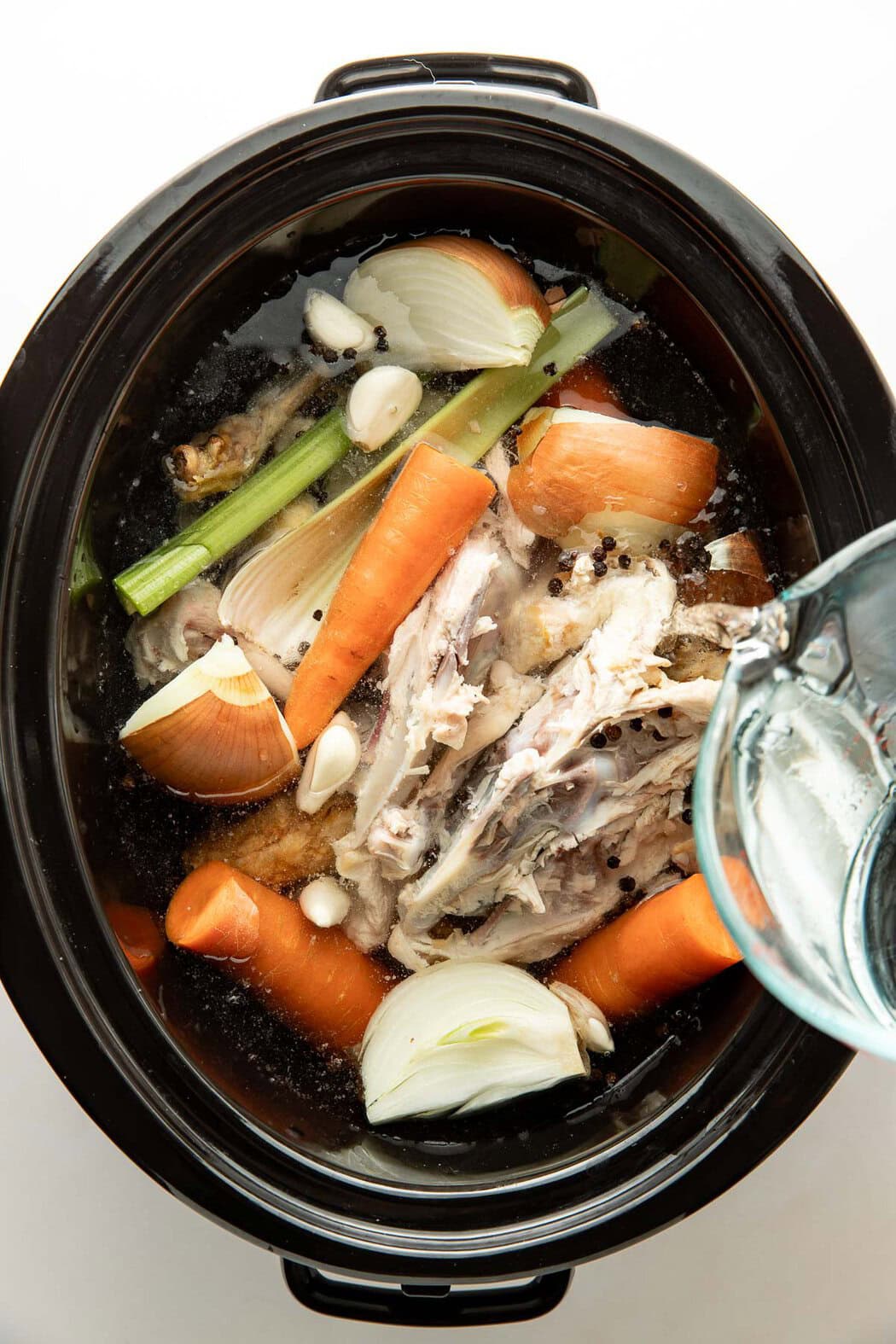 Overhead view of a slow cooker filled with bone broth ingredients including chicken bones and vegetables.
