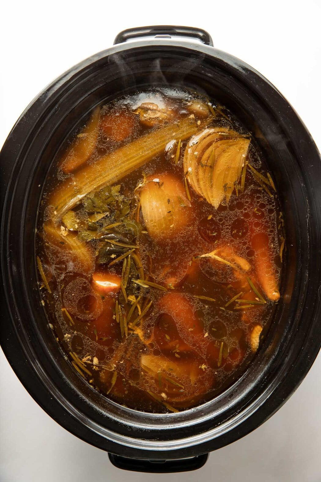 Overhead view a slow cooker filled with bone broth ingredients including chicken bones and vegetables.
