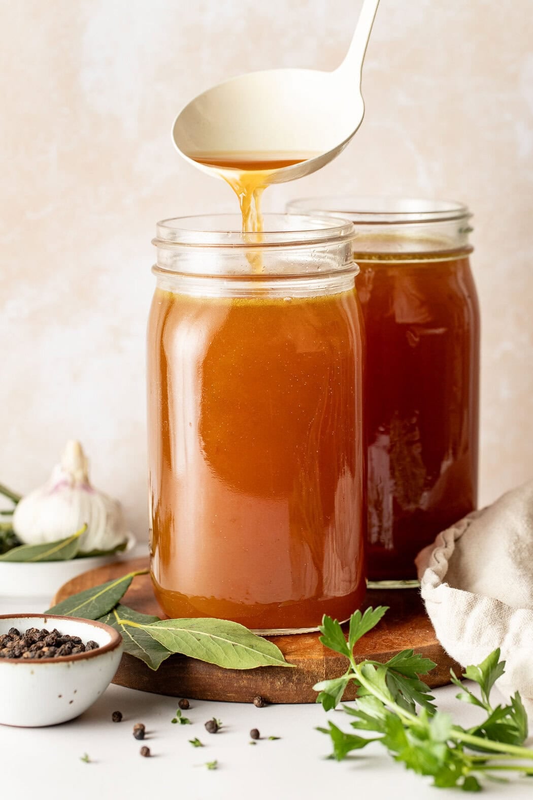 Close up view of two mason jars filled with rich bone broth on a wooden cutting board.