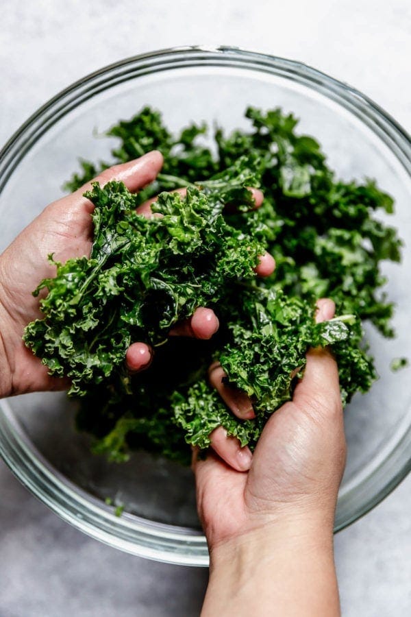 Overhead view of 2 hands massaging kale in a glass bowl. 