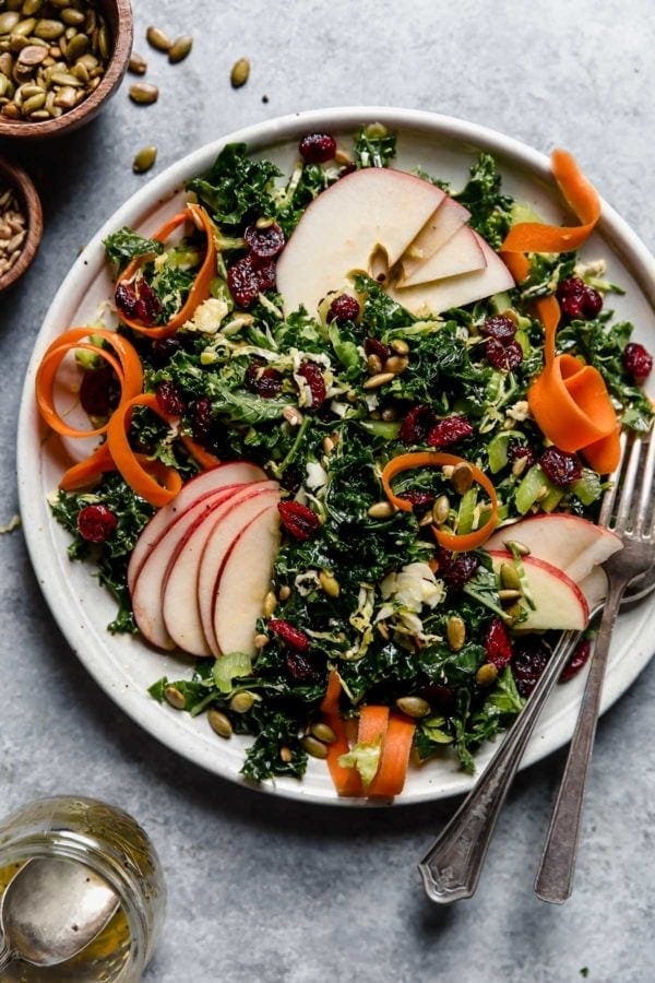 Overhead view of a plate of Massaged Kale Salad topped with sliced apples and carrots. 