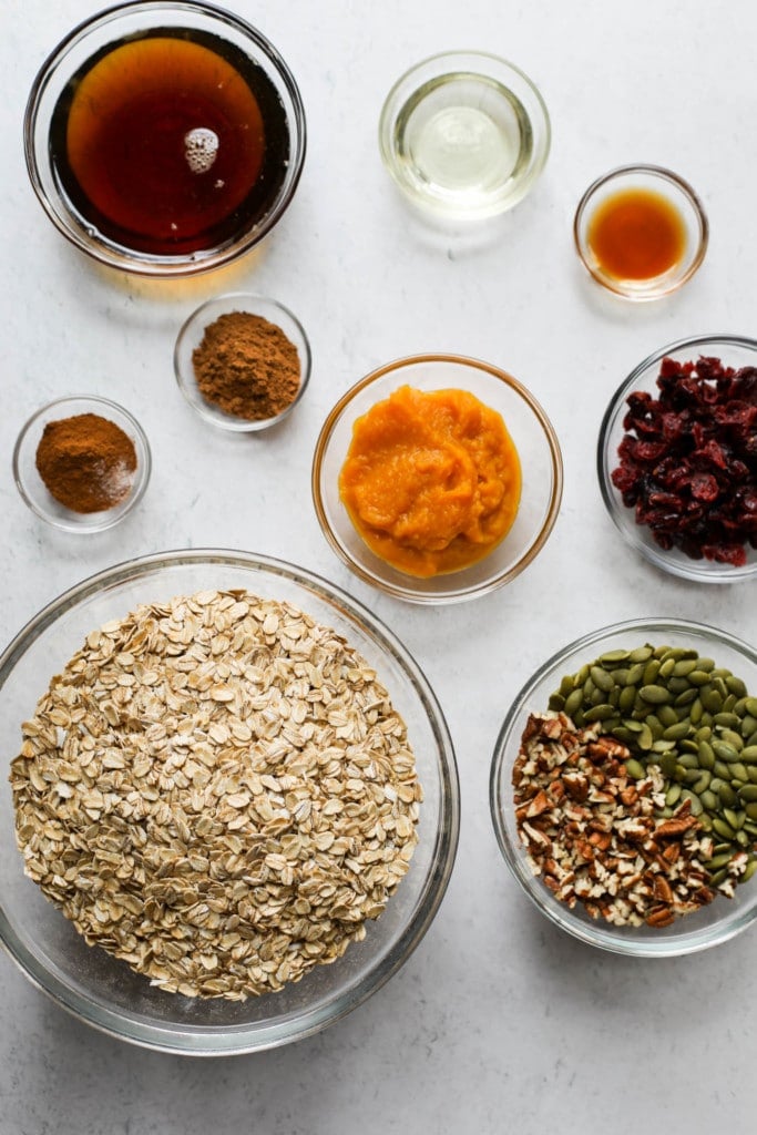 All ingredients for pumpkin spice granola in bowls arranged together in a cluster.