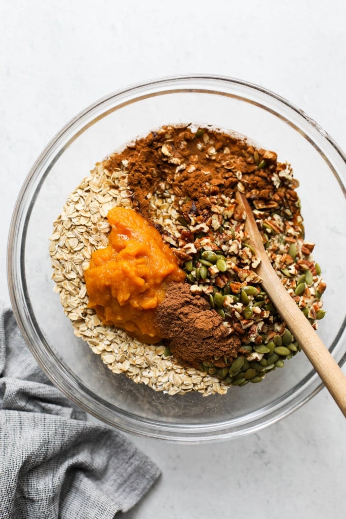 All ingredients for pumpkin spice granola in a mixing bowl with a wooden spoon