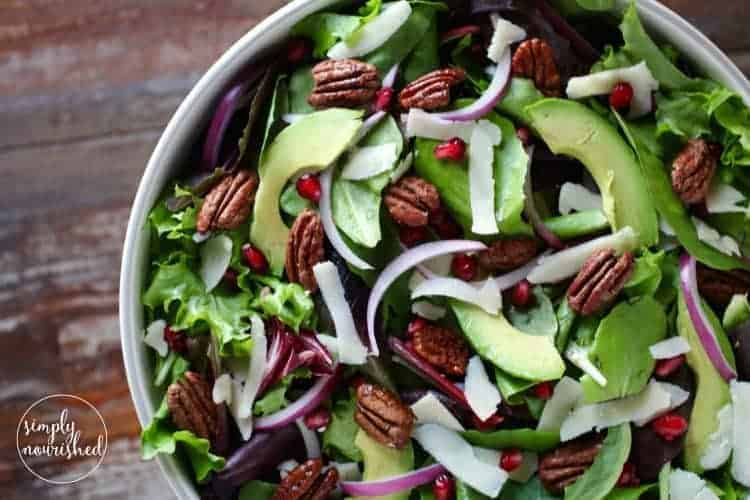 Close up view Pomegranate mixed greens salad with pecans, red onions, pomegranate arils, and shaved Parmesan.