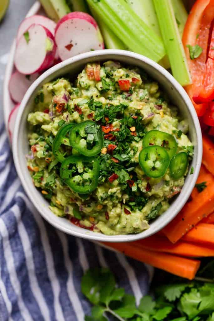 Overhead view of a bowl of guacamole surrounded by fresh raw vegetables