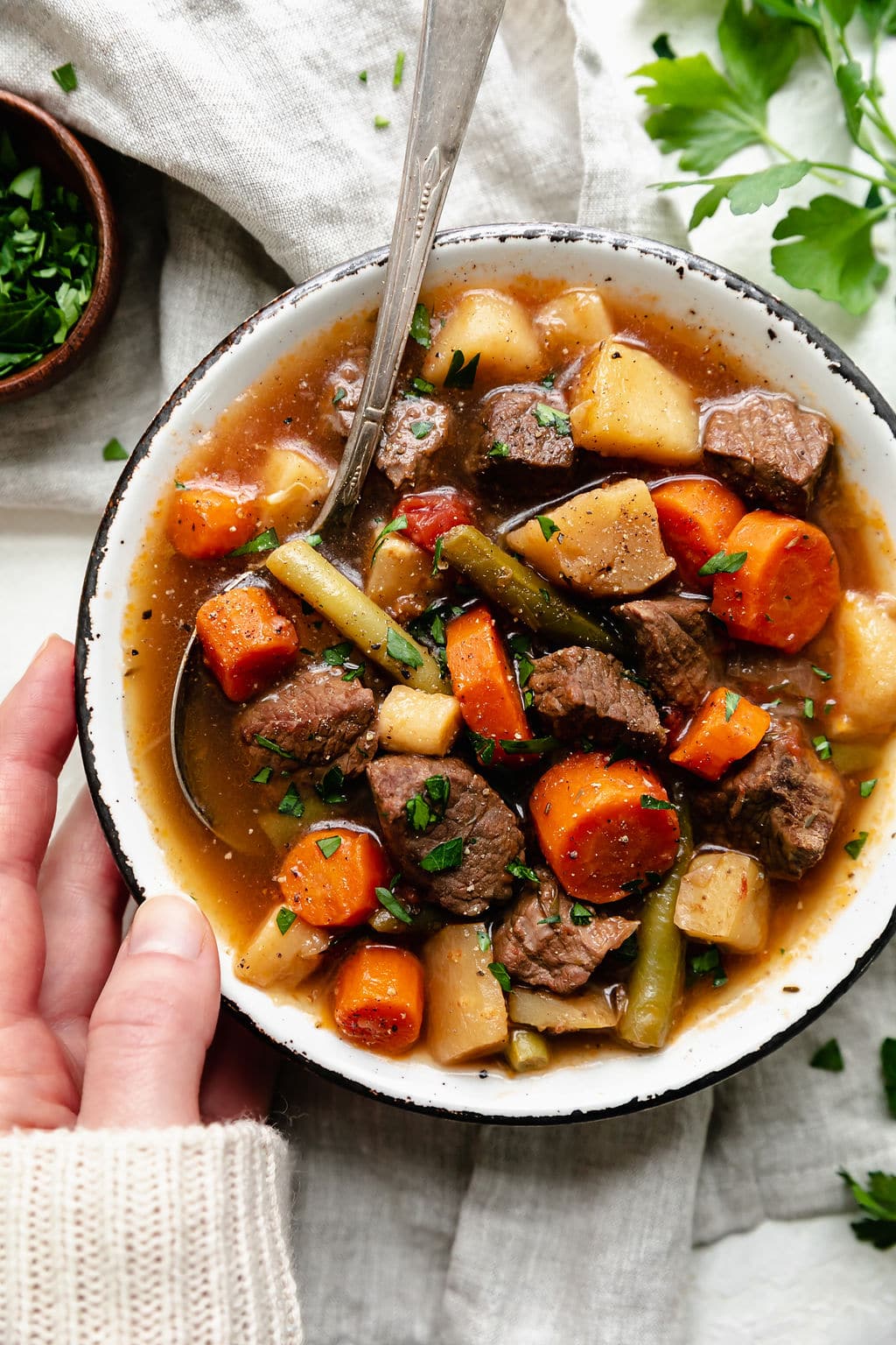 One hand resting against rustic bowl filled with slow cooker beef stew. 