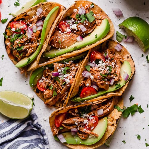 Several chicken tacos in corn shells with taco toppings.