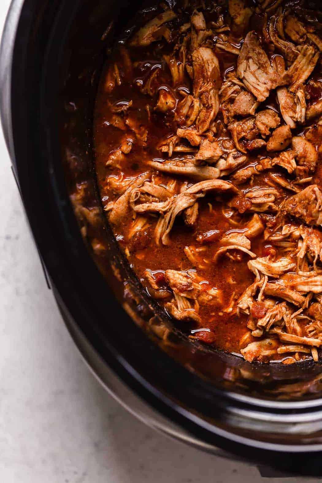Overhead view shredded chicken for tacos in sauce.