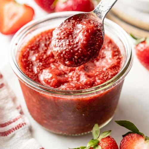 Overhead view of a small jar of red Chia Seed Jam with a spoon bringing up a scoop.