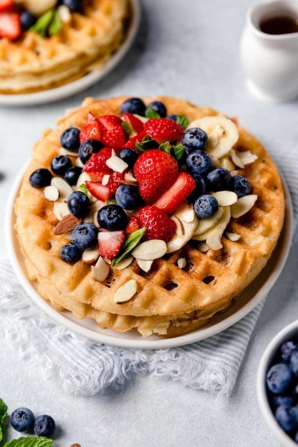 Overhead view of a plate of Crispy Grain-Free Waffles topped with fresh berries and sliced almonds.