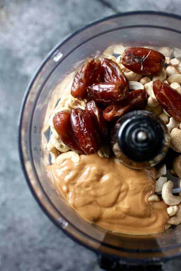 Overhead shot of food processor filled with dates, nut butter and cashews, the ingredients for the Nutty Cashew Bites. 