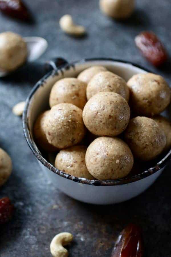 Photo of Nutty Cashew Bites in a white tea cup with dates and cashews surrounding. 