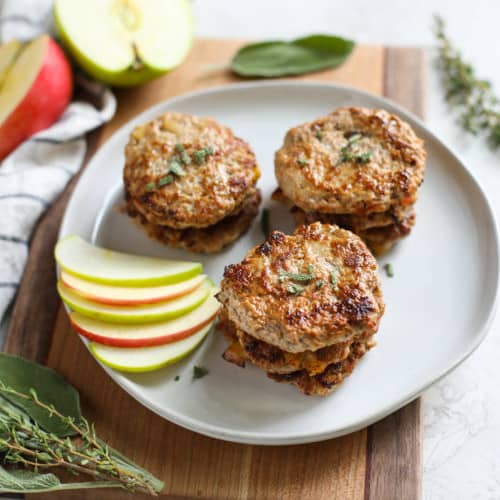 Turkey sausage patties on a white plate with a side of sliced apples