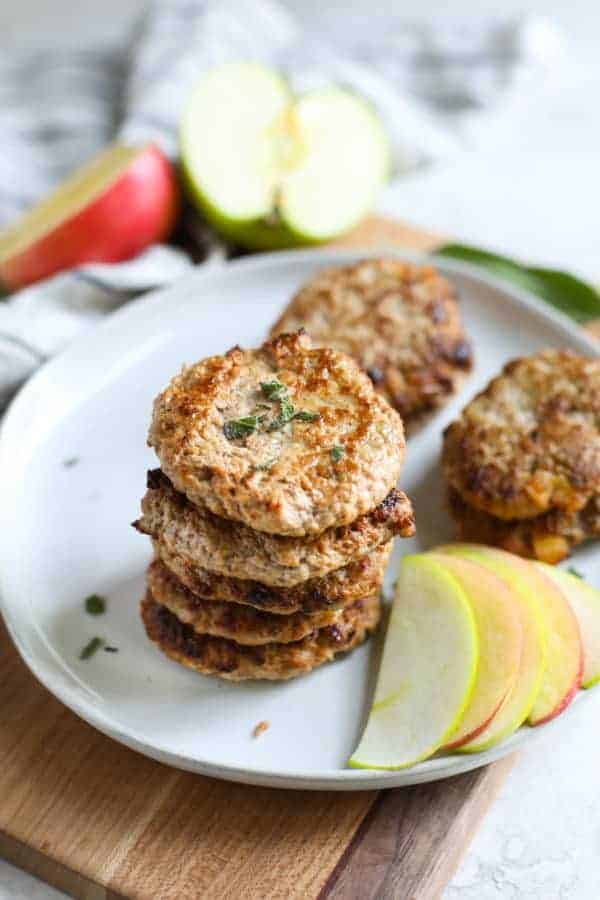 Turkey Apple Sausage Patties stacked on a white plate with a side of apple slices