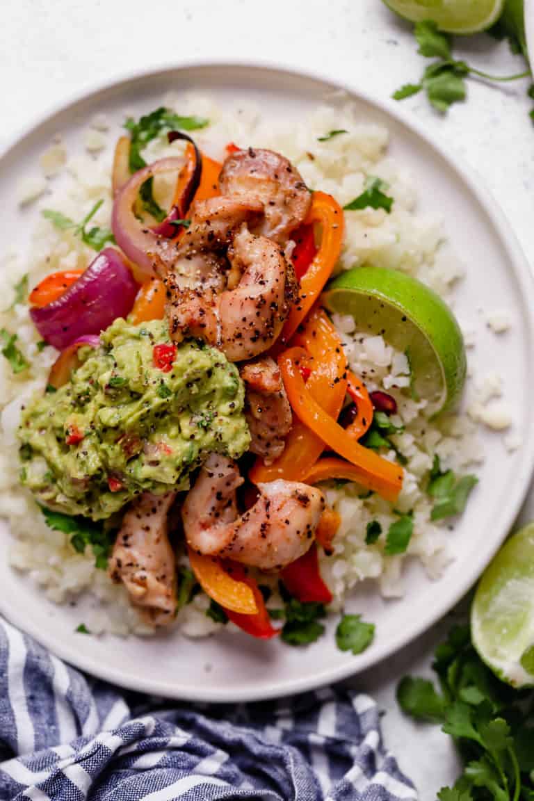 Overhead view of a plate of chicken fajitas on top of cauliflower rice and topped with a dollop of guacamole.