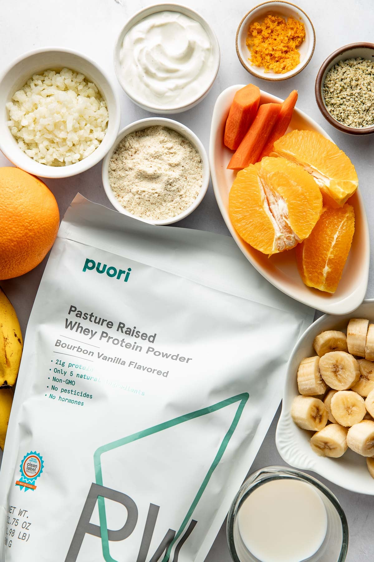 Overhead view of a variety of ingredients for an orange smoothie including a bag of protein powder.