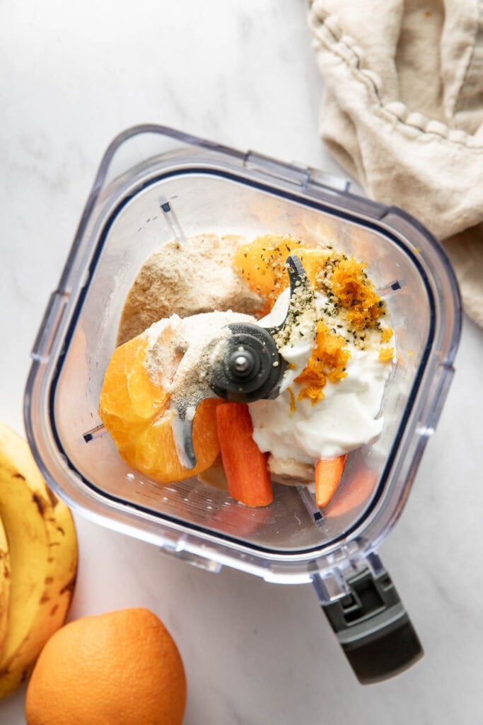 Overhead view of the inside of a blender filled with orange smoothie ingredients ready for blending.