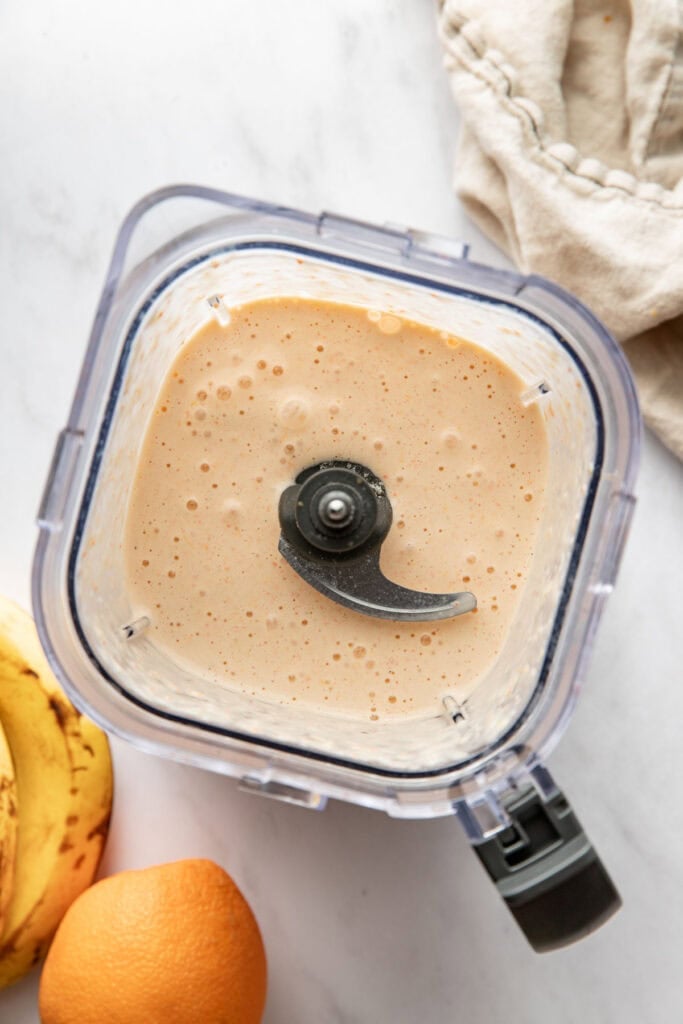 Overhead view of a blender filled with freshly blended orange smoothie ready for drinking.