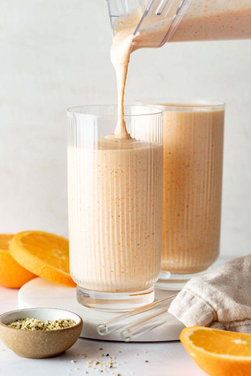 Close up view of two glasses filled with orange smoothie next to freshly cut oranges.