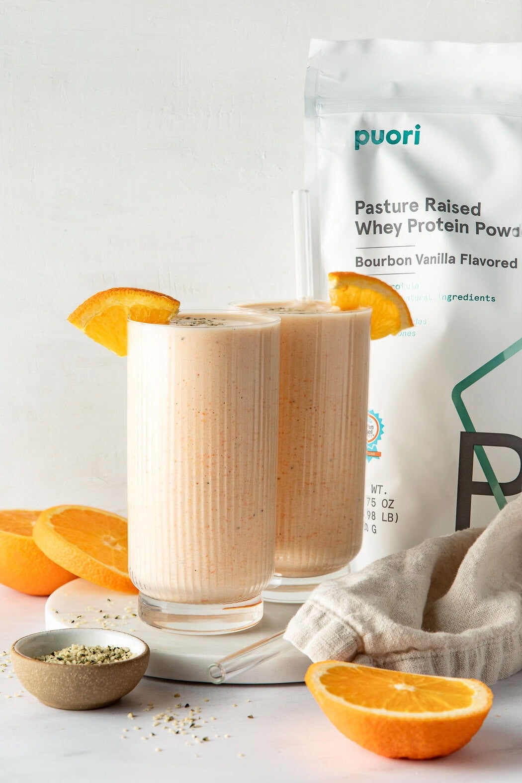 Close up view of two orange smoothies topped with orange slices and sprinkled with hemp hearts.