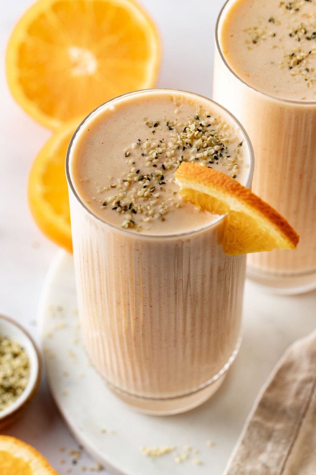 Overhead view of an orange smoothie in a glass topped with an orange slice and sprinkled with hemp hearts.