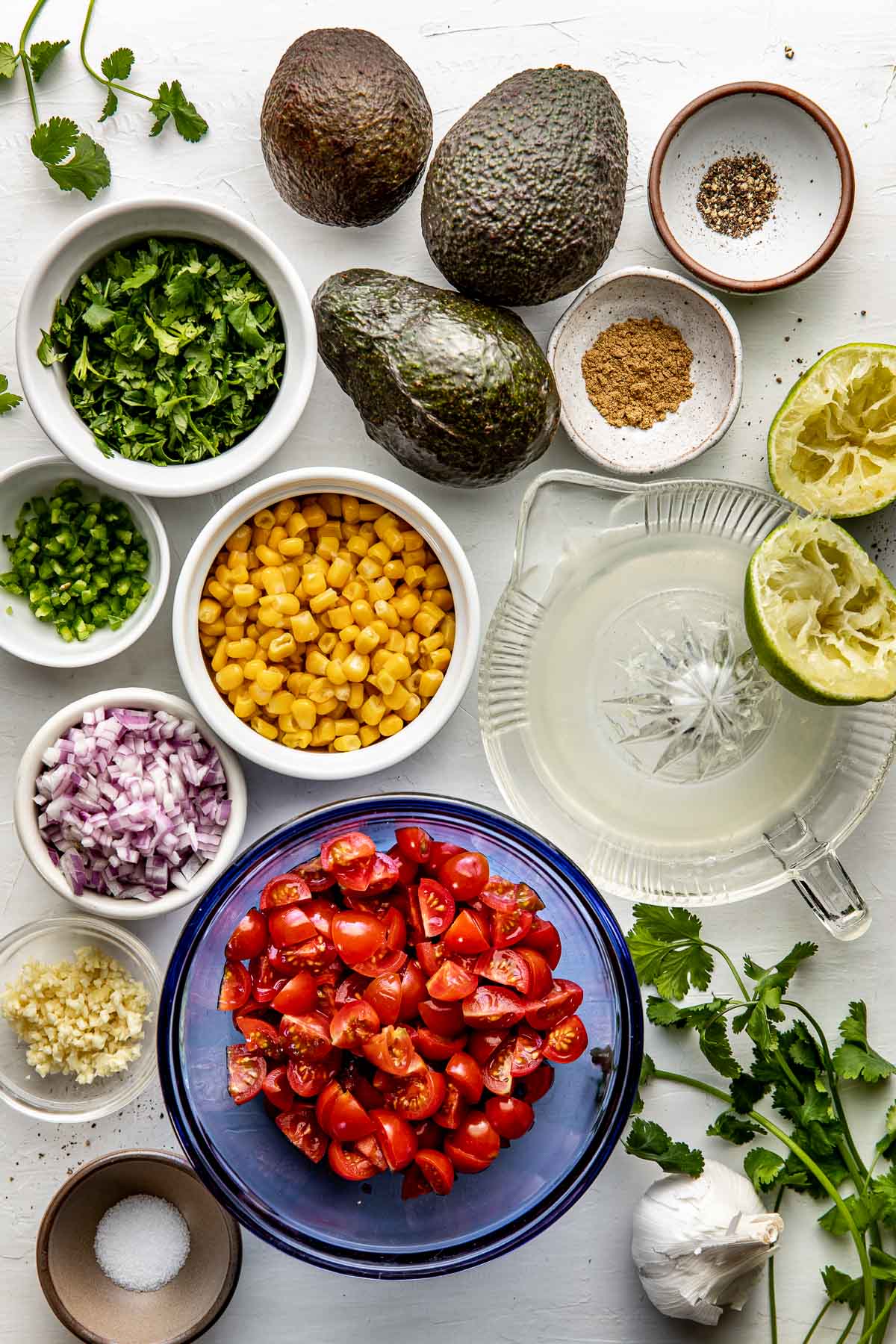 Overhead view of a variety of ingredients for Avocado Salsa in different sized bowls. 