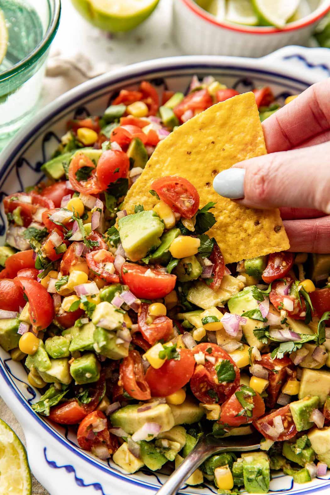 Close up view of a hand scooping a yellow tortilla chip into a bowl of Avocado Salsa