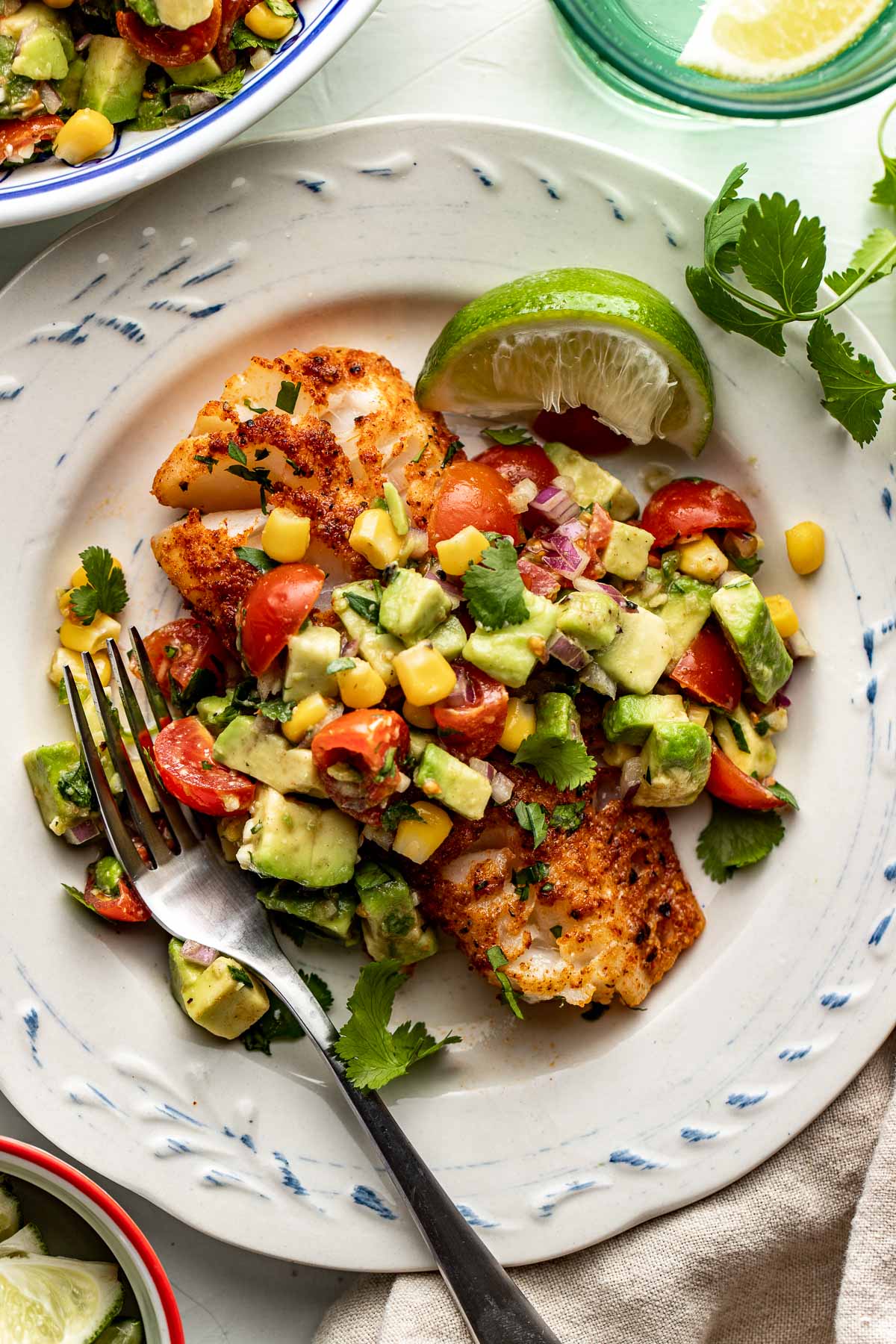Close up view of a plate of seasoned cod topped with colorful Avocado Salsa and fresh cilantro