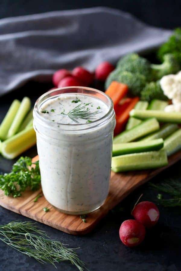 Close up view of a mason jar filled with Paleo Ranch Veggie Dip and raw vegetables in the background. 