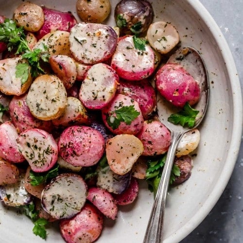 Garlic roasted radishes plated on a cream plate topped with ranch dressing and fresh herbs