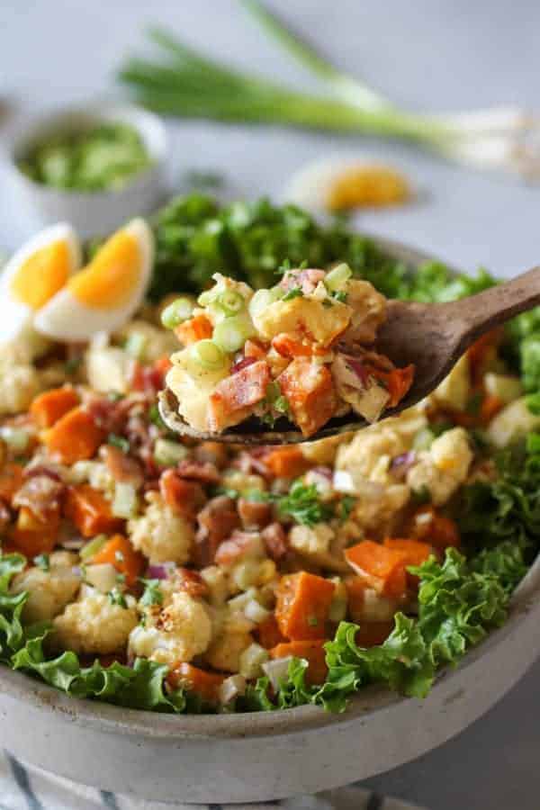 Roasted Cauliflower Sweet Potato Salad in a bowl with some on a wooden spoon being lifted towards the camera