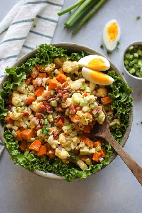 Roasted Cauliflower Sweet Potato Salad ingredients in a bowl and some resting on a wooden spoon on top