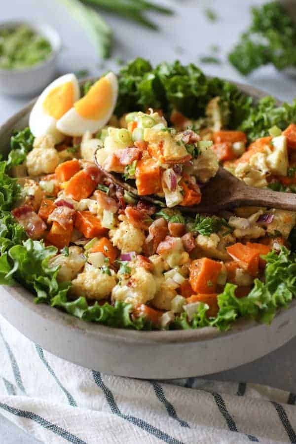 Cauliflower Sweet Potato Salad with Bacon in a bowl and on a wooden spoon resting on top