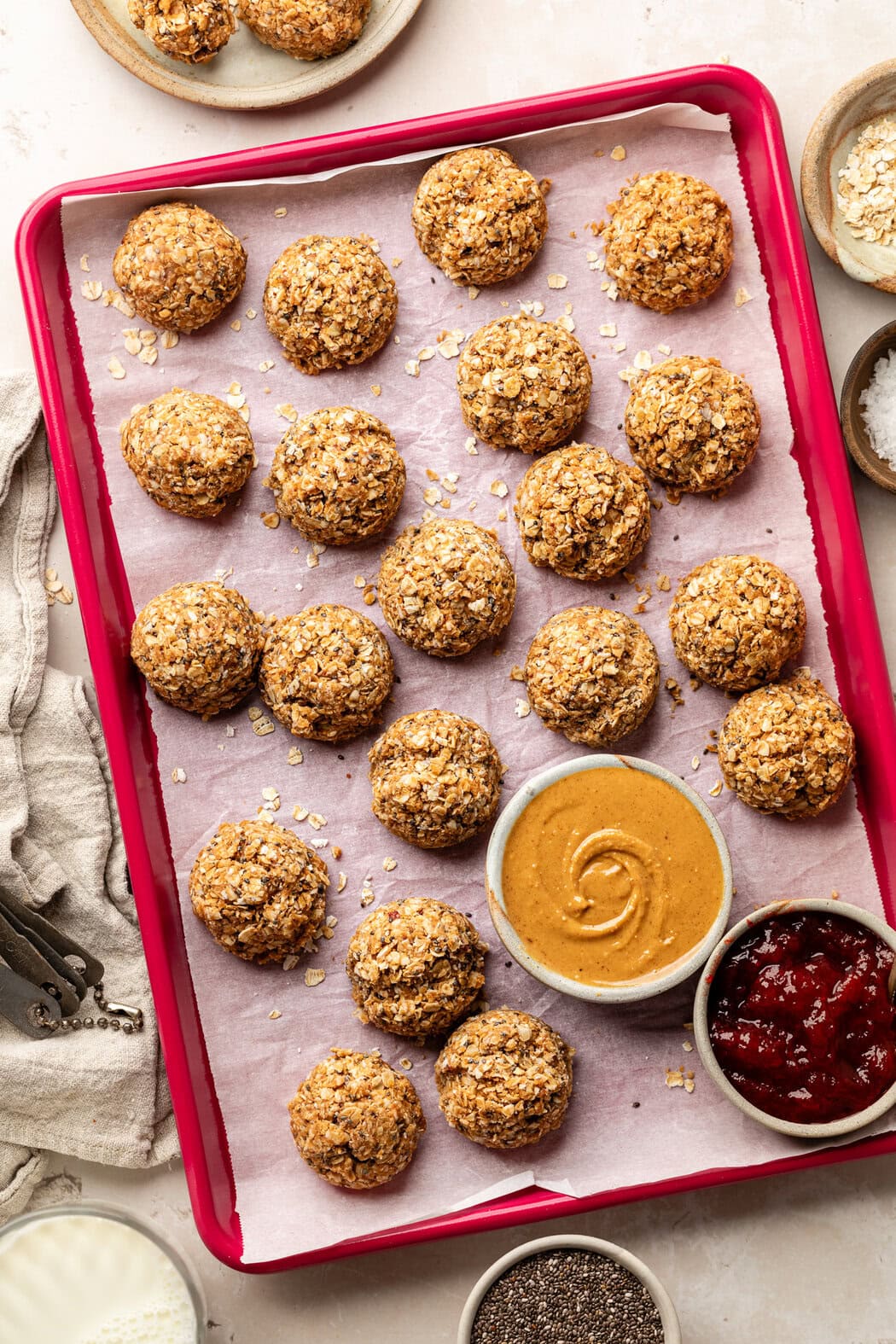 Overhead view of a red sheet pan filed with No-Bake PB & J Bites and bowls of peanut butter and jelly on the side. 