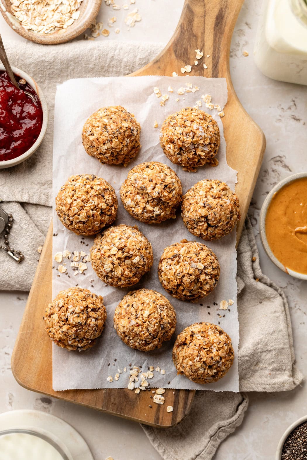 Overhead view of a wooden cutting board filled with No-Bake PB & J Bites topped with chia seeds and oat pieces. 