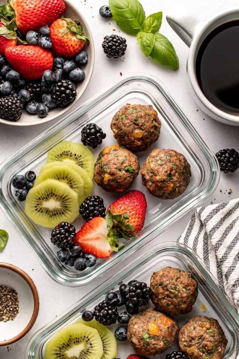 Overhead view of two glass meal prep containers filled with apricot basil breakfast meatballs and fresh colorful fruit.