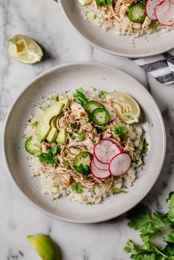 Overhead view of 2 bowls of Chile Chicken Verde topped with sliced radishes, jalapenos, and avocado