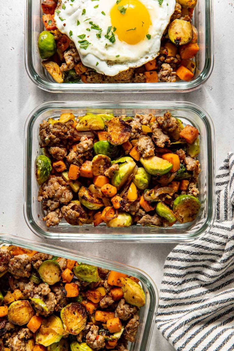 Overhead view of glass meal prep containers filled with sweet potato sausage hash and topped with a fried egg.