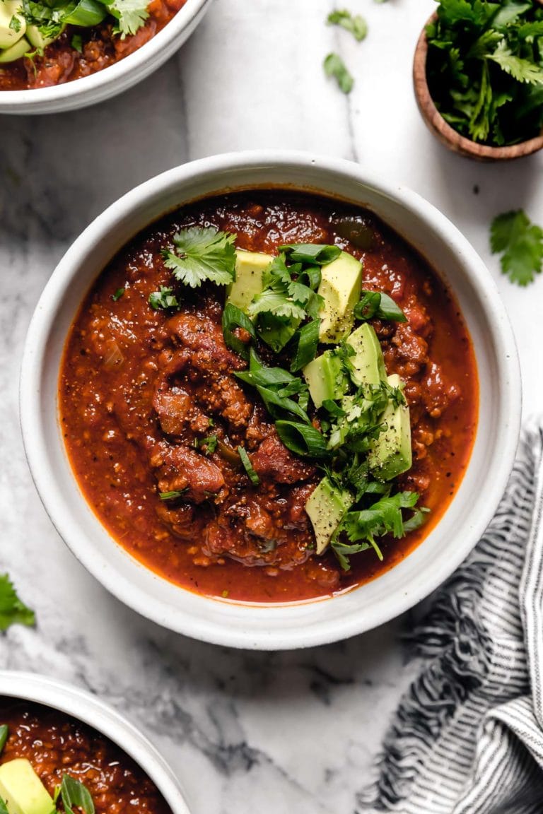 Overhead view of a small white ceramic bowl of Slow Cooker Pumpkin Chili topped with avocado and cilantro