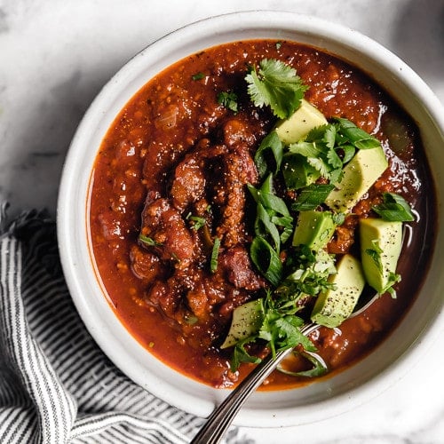 An overhead view of a white bowl filled with Slow Cooker Pumpkin Chili that's topped with diced avocado, fresh cilantro, and sliced green onions.