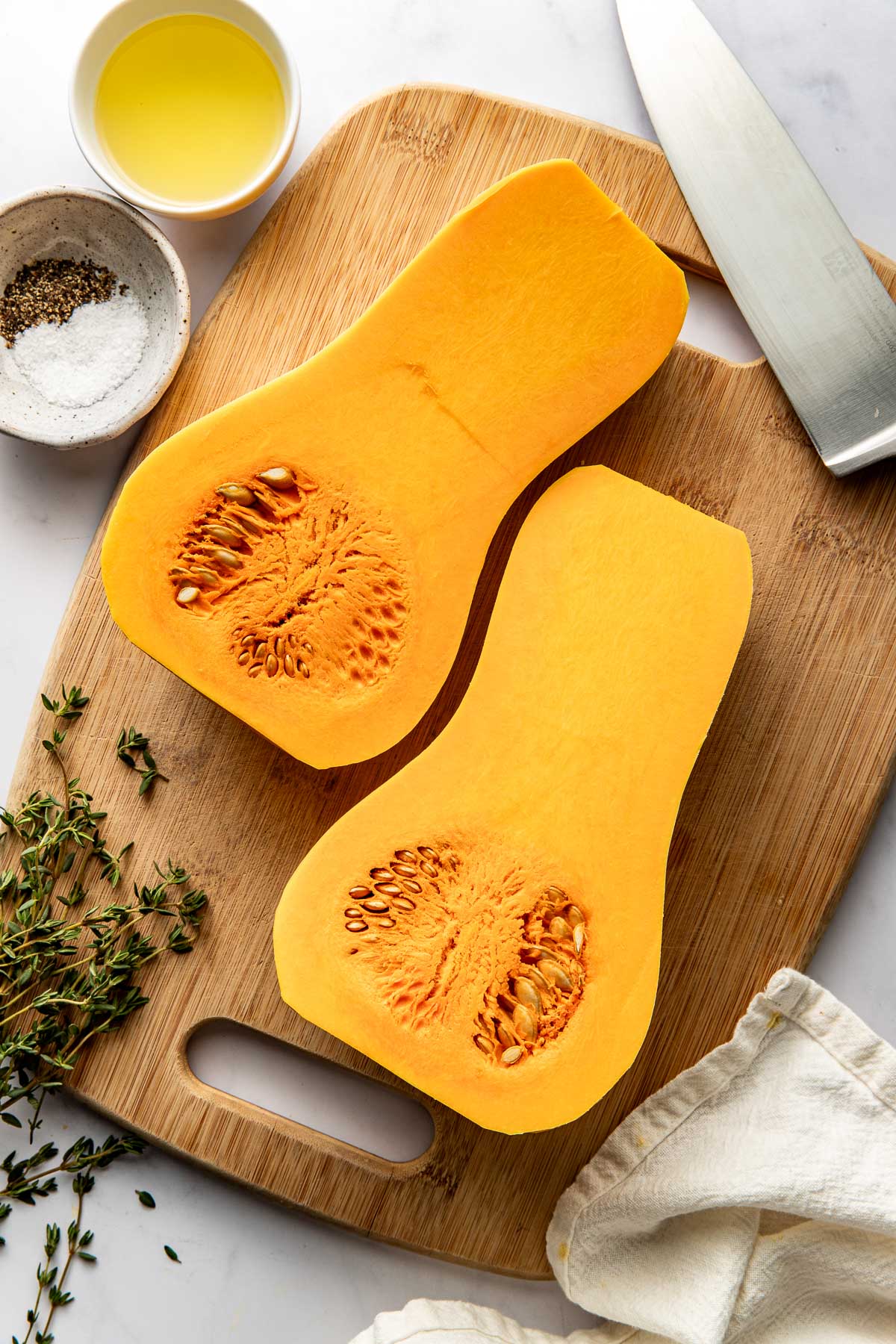 Overhead view of a wooden cutting board with a butternut squash on top cut in half. 
